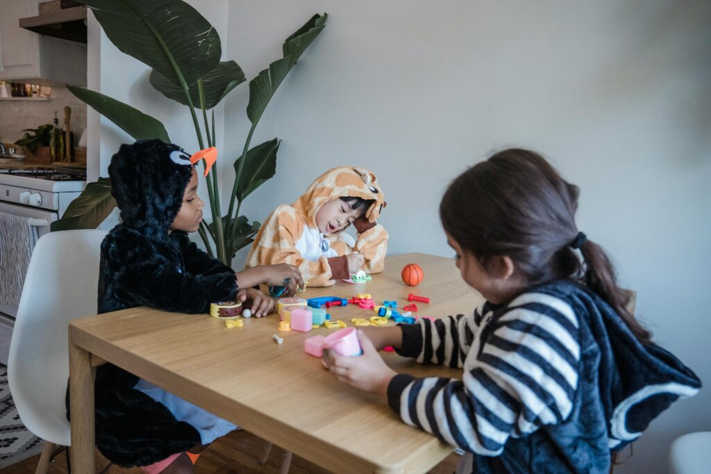 Three kids in animal onesies play with colorful kids toys at a table indoors, having fun and exploring creativity